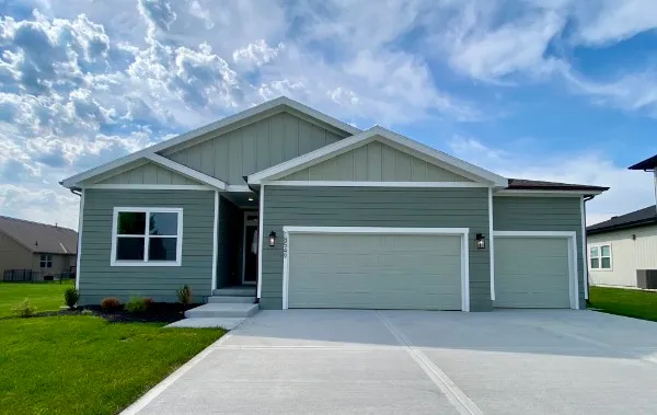 Sage green one-story house with two-car garage, front entry, and concrete driveway on green lawn.