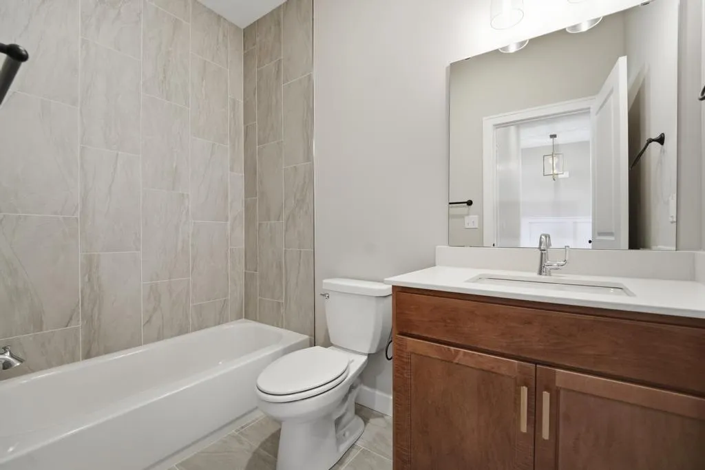 Bathroom with wood vanity, white countertop, large mirror, toilet, and bathtub with gray tile surround.