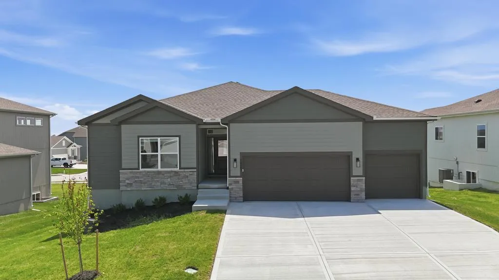 Gray ranch-style home with dual-car garage, stone accents, and concrete driveway on landscaped lot.