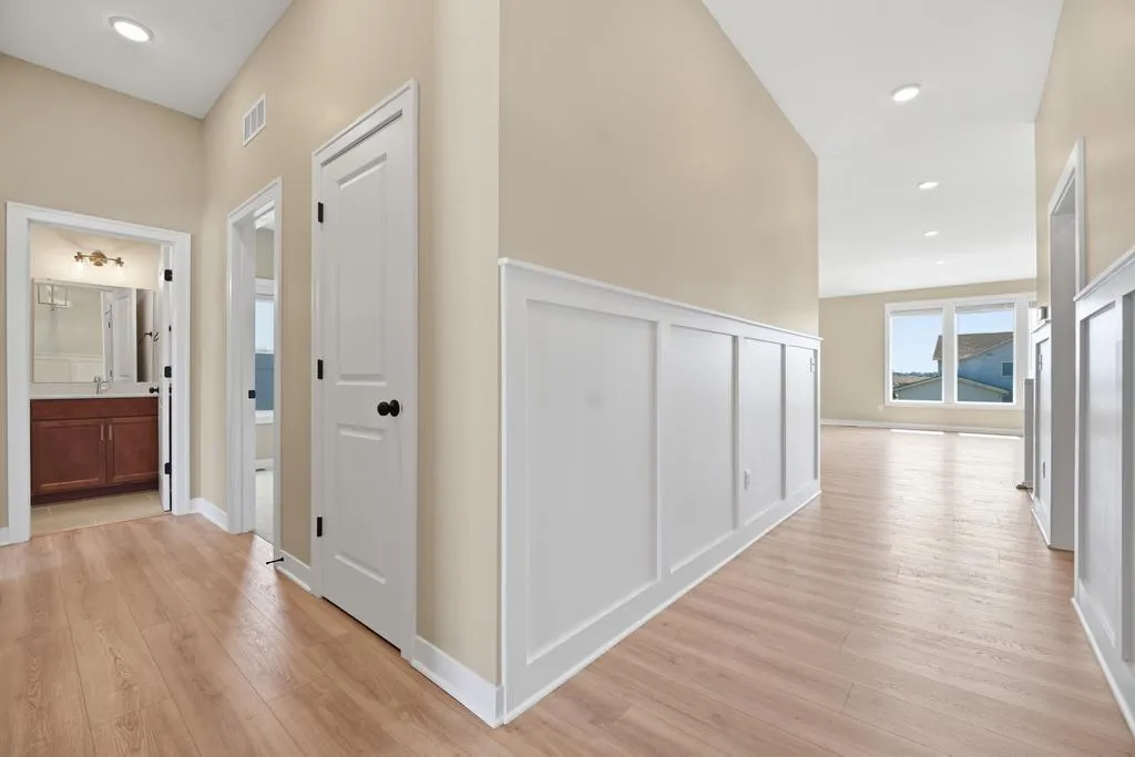 Master bedroom hallway with beige walls, white doors, wood flooring, and windows overlooking landscape views.
