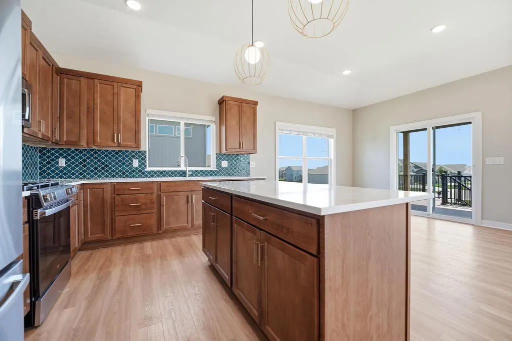 Kitchen with wood cabinets, white countertops, blue tile backsplash, island, and glass doors opening to a deck.