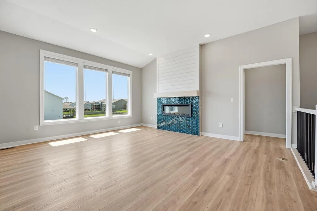 Open living room with wood flooring, three-window wall, fireplace with blue tile surround, and white shiplap accent wall.