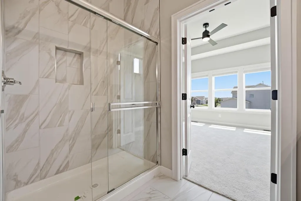 Master bathroom with glass walk-in shower and open door leading to bedroom with patio access.