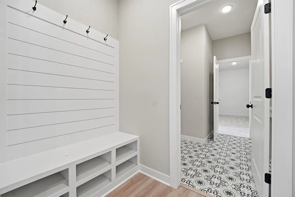 Mudroom with white shiplap wall, built-in bench with storage cubbies, black hooks, and patterned tile flooring leading to