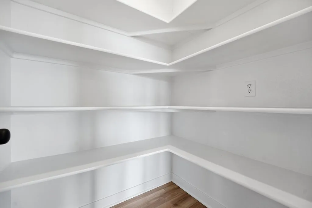 Empty white pantry with built-in shelving, recessed ceiling lighting, and wood flooring.