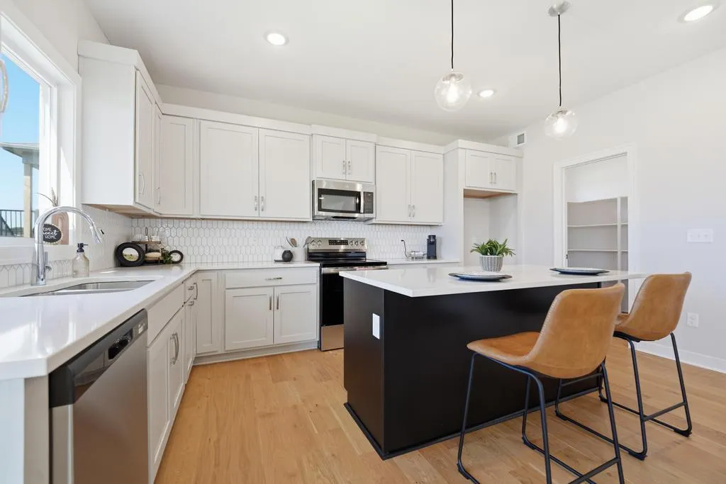 White kitchen with white cabinetry, white subway tile backsplash, black island with white countertop, stainless steel