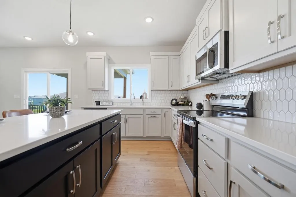 Kitchen with white upper cabinets, dark island with white countertop, stainless steel appliances, hexagonal tile backsplash,