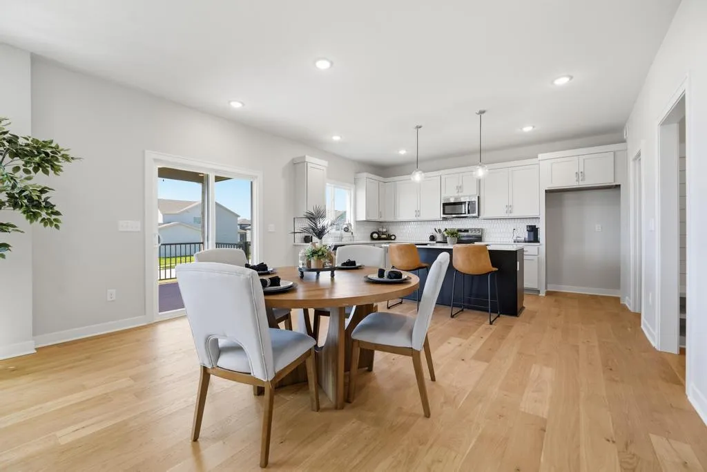 Open dining and kitchen area with wooden table, white cabinetry, island seating, and glass doors opening to a balcony.