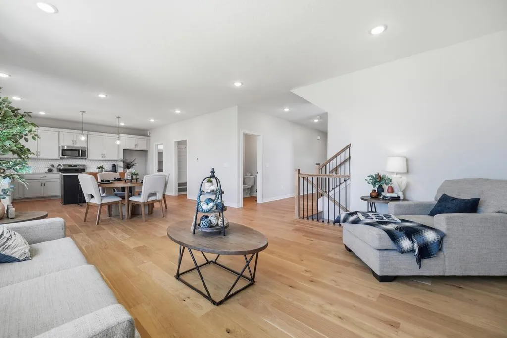 Open-concept living space with white cabinetry, gray upholstered furniture, wooden flooring, and stairs with metal railings.