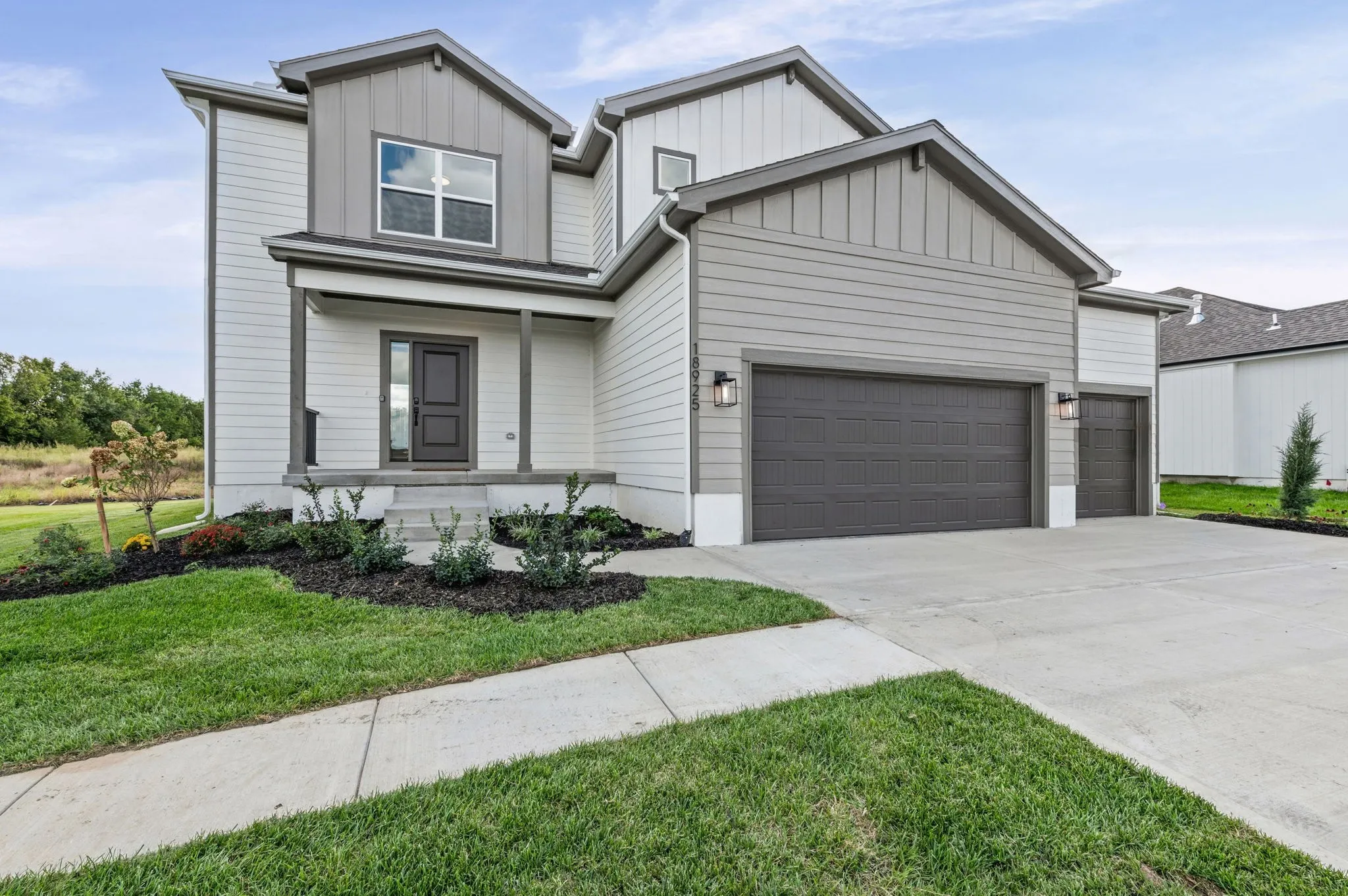 Two-story home with white siding, dark gray garage doors, front porch, and landscaped lawn.