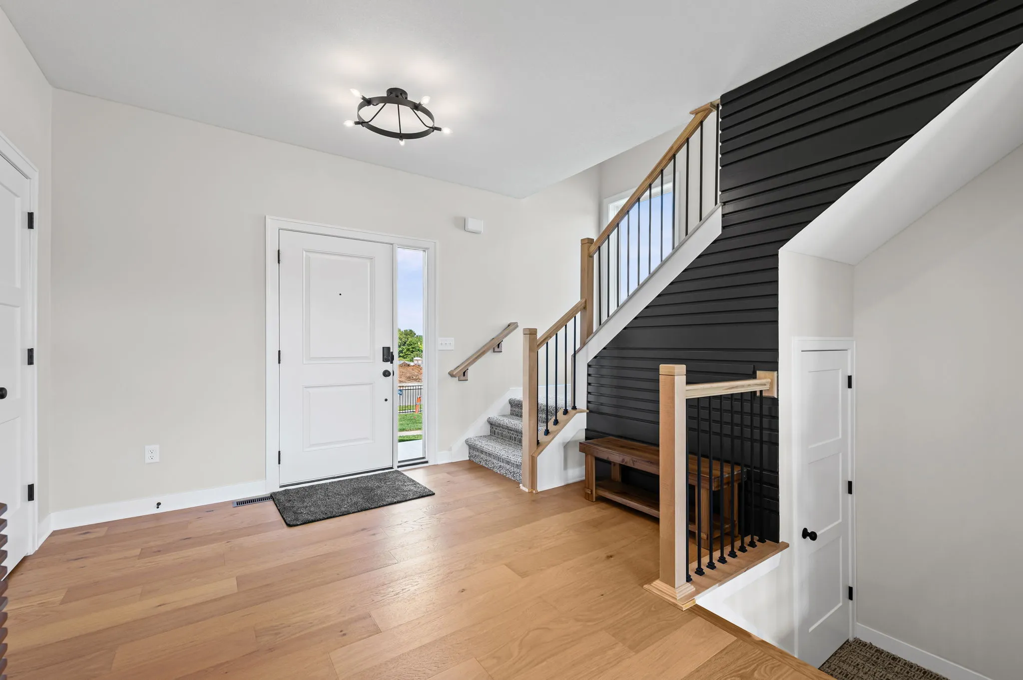 Foyer with wood flooring, white walls, staircase with wood railing and black shiplap accent wall, and white front door.