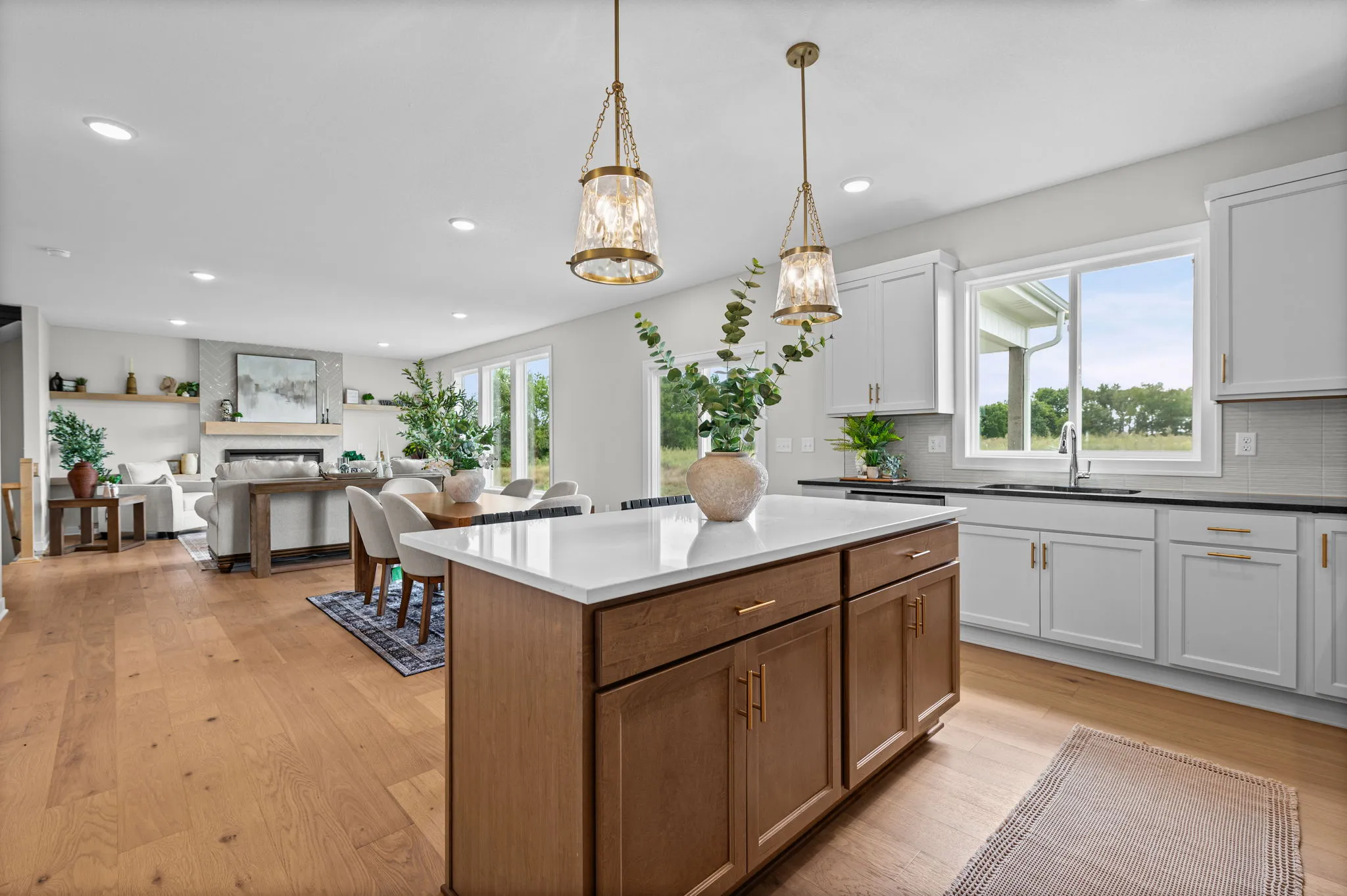 Open kitchen with white cabinetry, wood island with white countertop, pendant lights, and view to living room and windows.