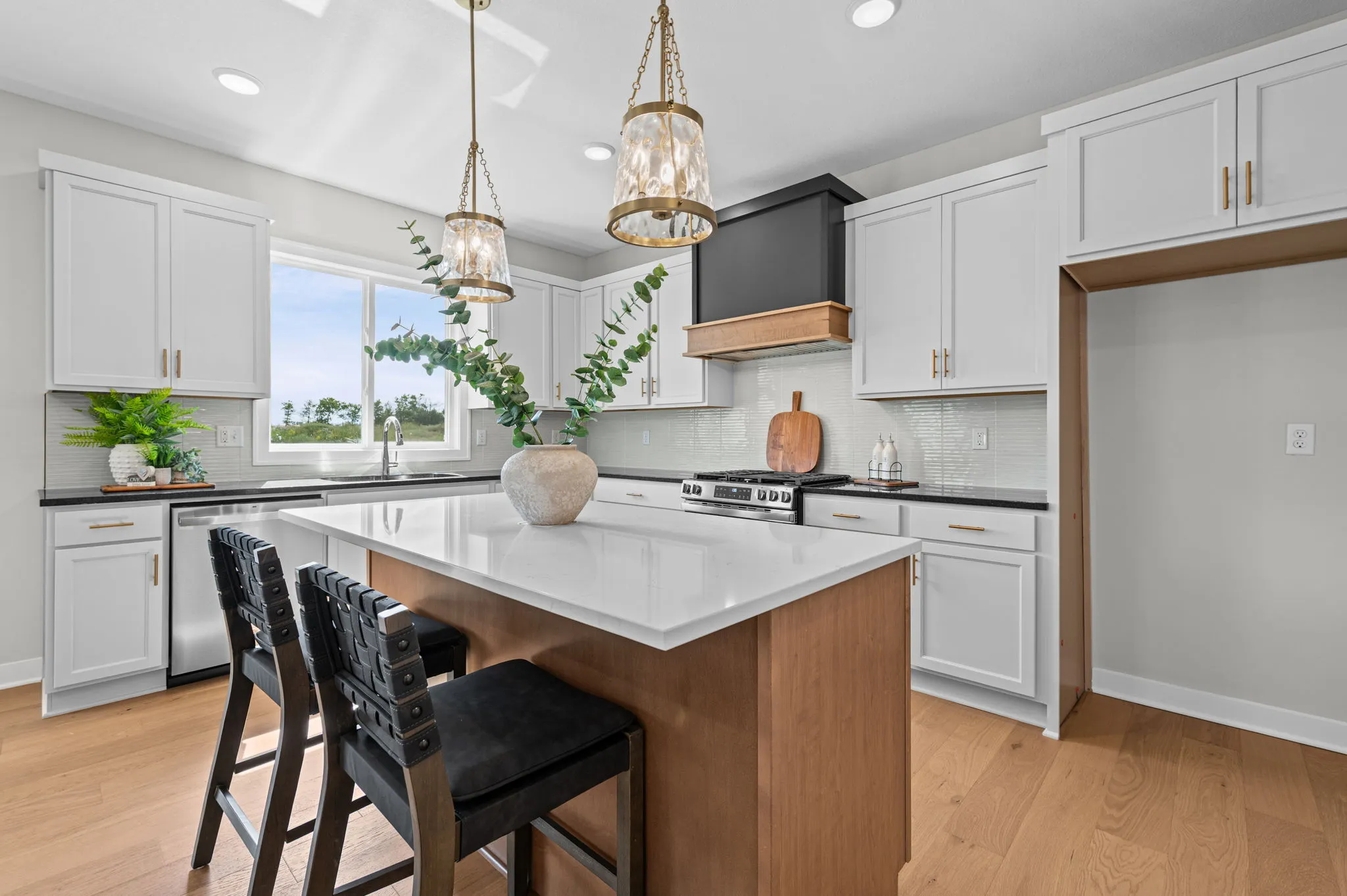 Kitchen with white cabinetry, wood island with white countertop, black bar stools, pendant lights, and white subway tile