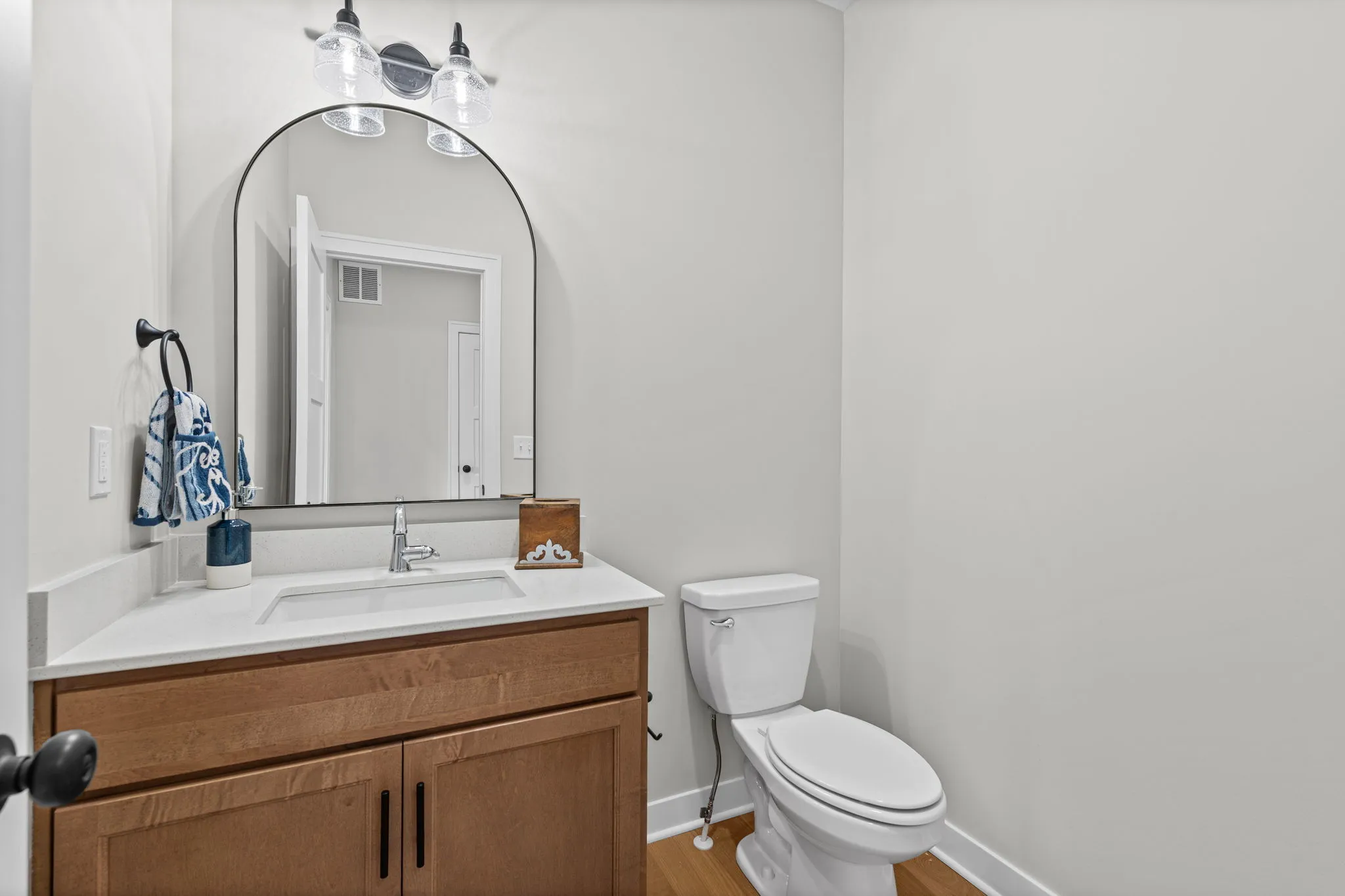 Bathroom with wood vanity cabinet, white countertop, arched mirror with sconces, and white toilet.