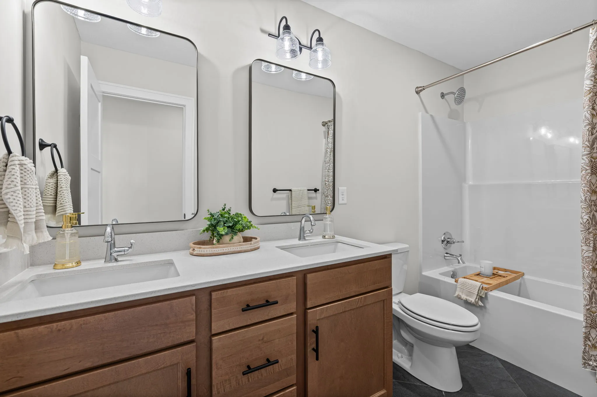 Bathroom with double vanity with white countertop and wood cabinetry, framed mirrors, and bathtub with shower enclosure.