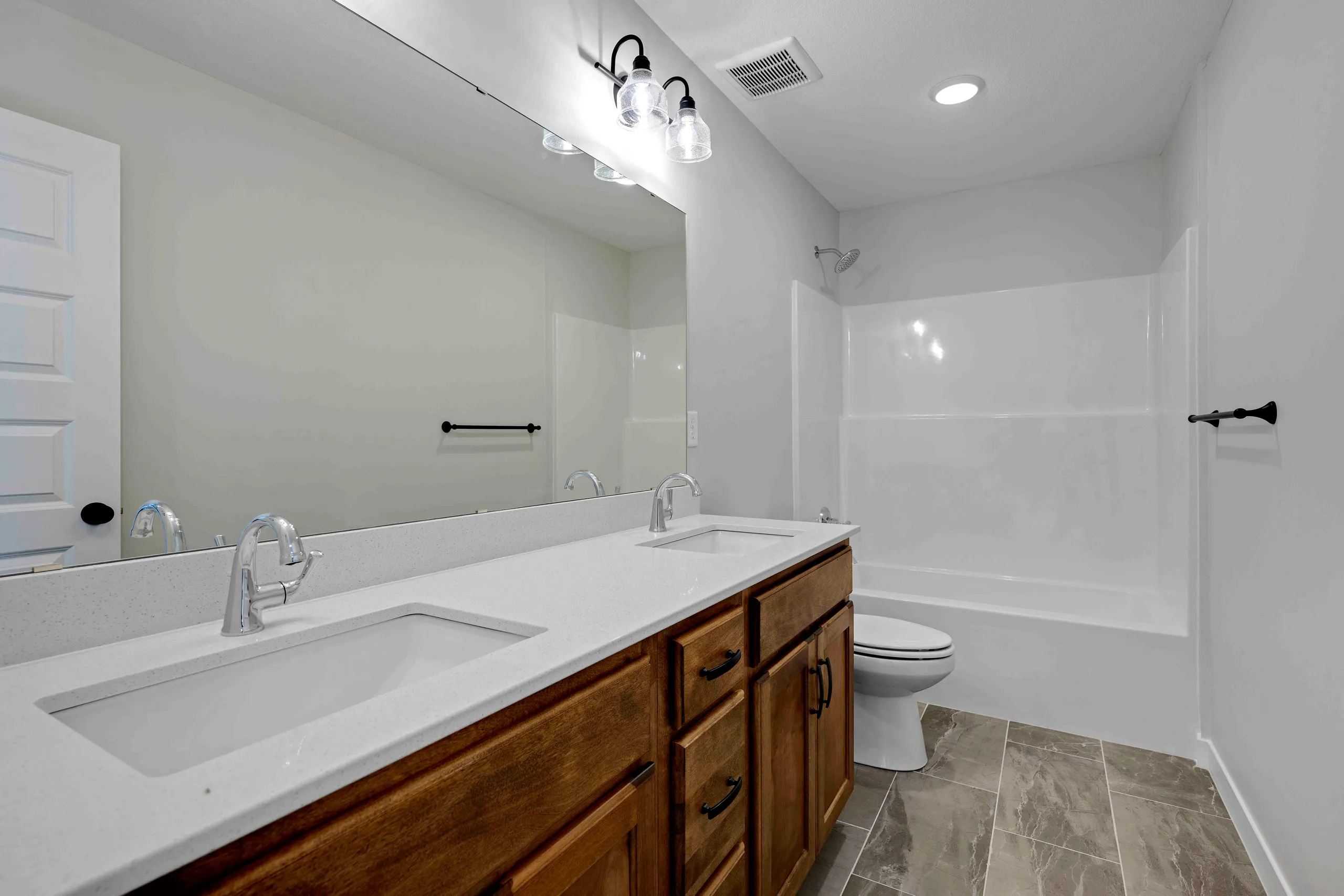 Bathroom with double vanity with white countertop and wood cabinetry, large mirror, black fixtures, and walk-in shower with