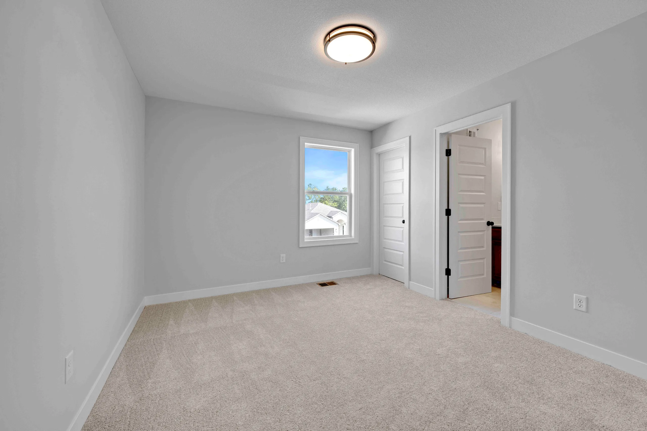 Empty bedroom with gray walls, beige carpet, window with outdoor view, and two white closet doors.