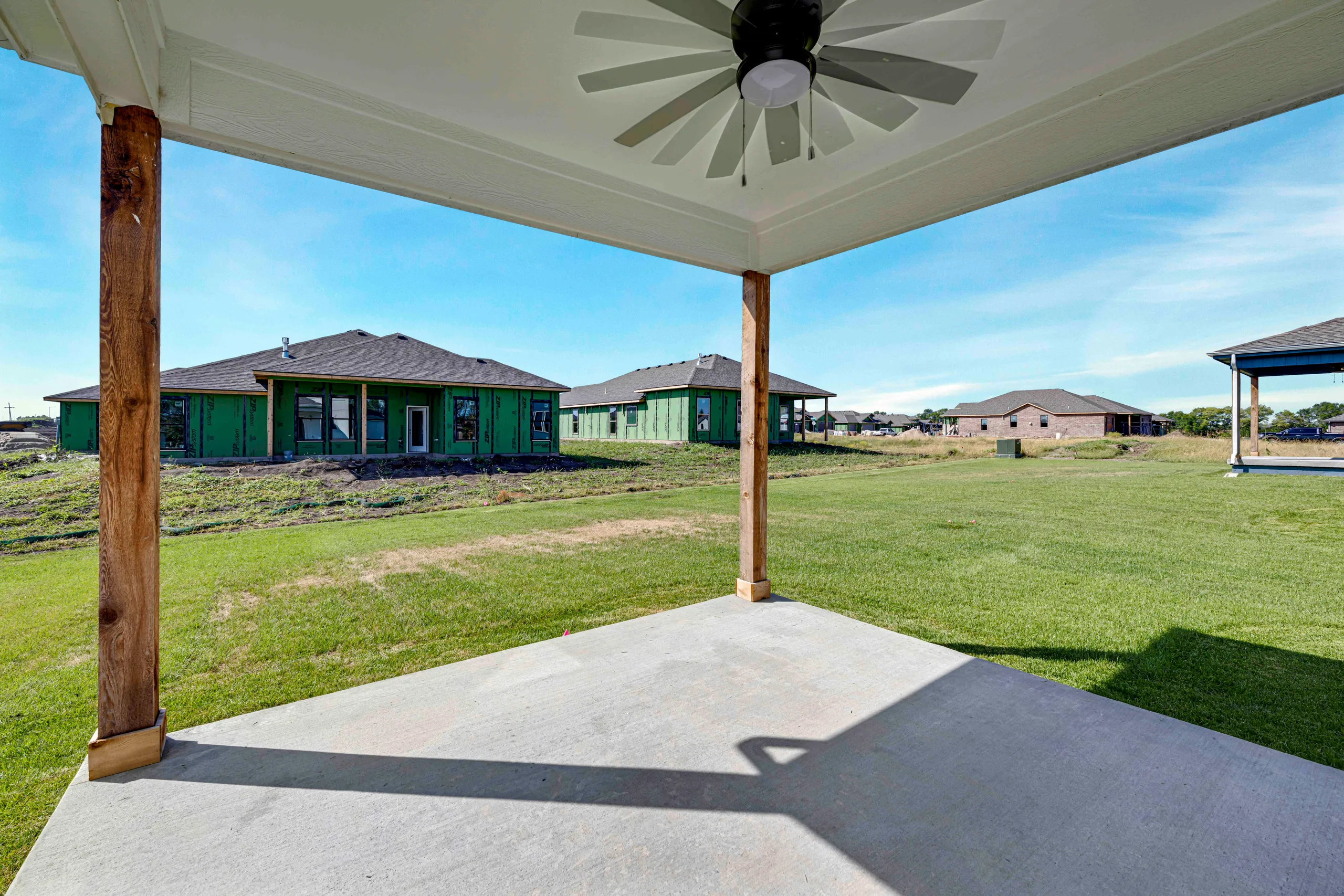 Covered patio with ceiling fan overlooking green lawn and neighboring homes in a rural community.