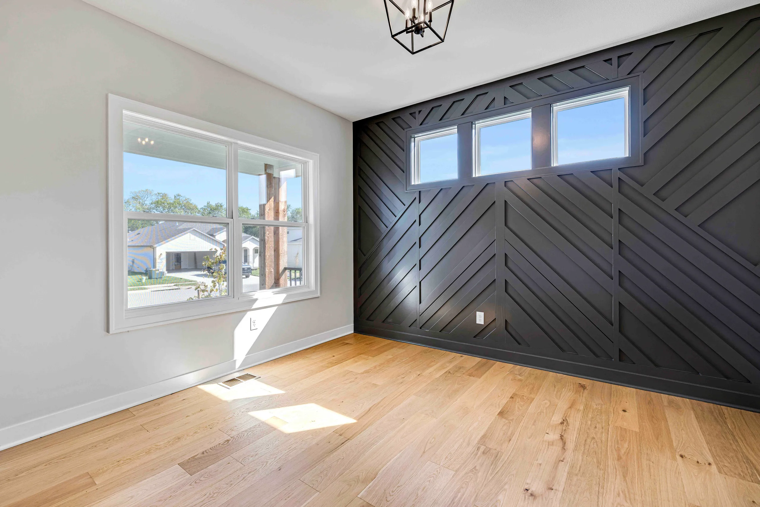 Room with wood plank flooring, white drywall, dark diagonal shiplap accent wall, windows, and geometric ceiling fixture.