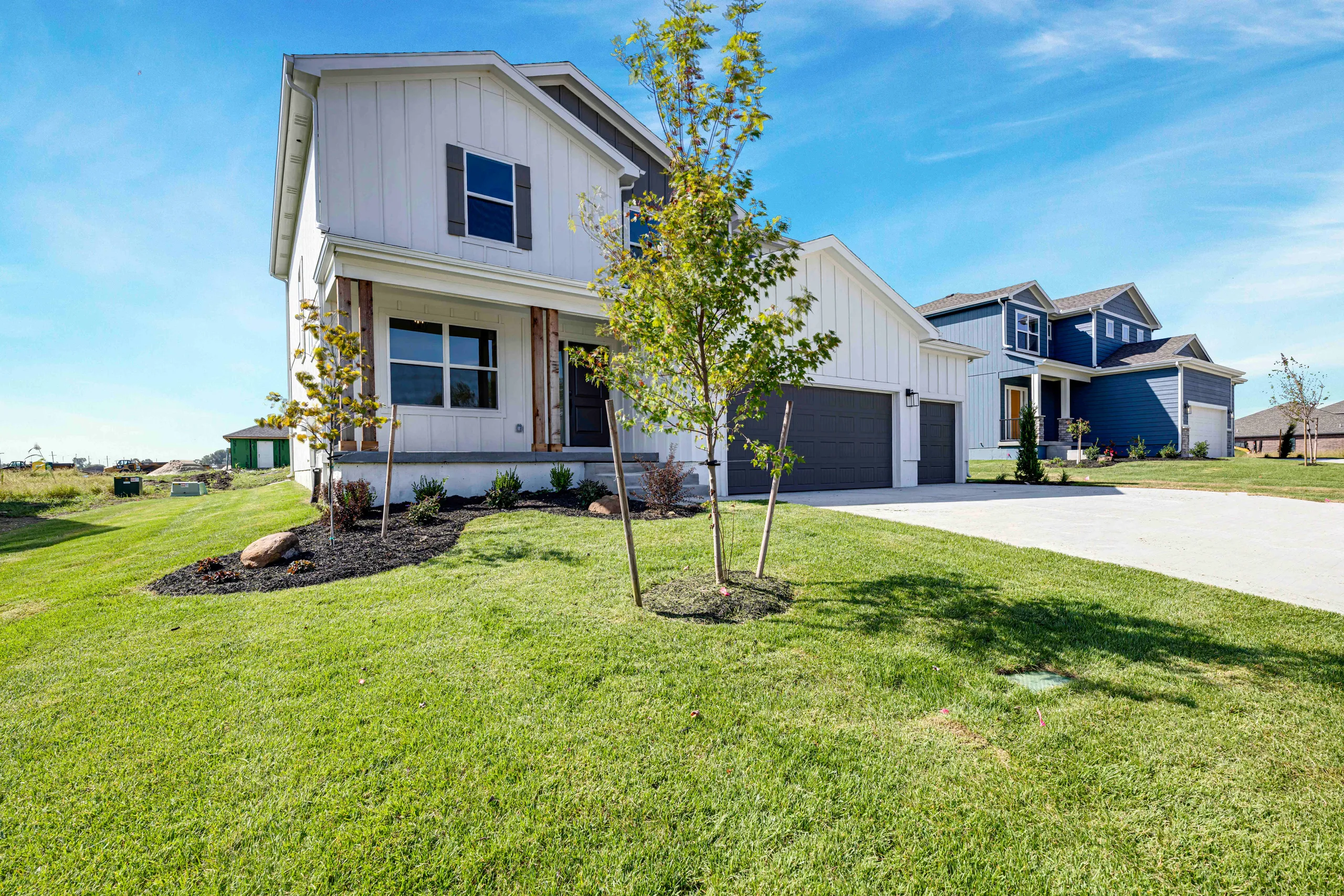 Two-story white and blue house with dark garage doors, young landscaping, and driveway in suburban community.