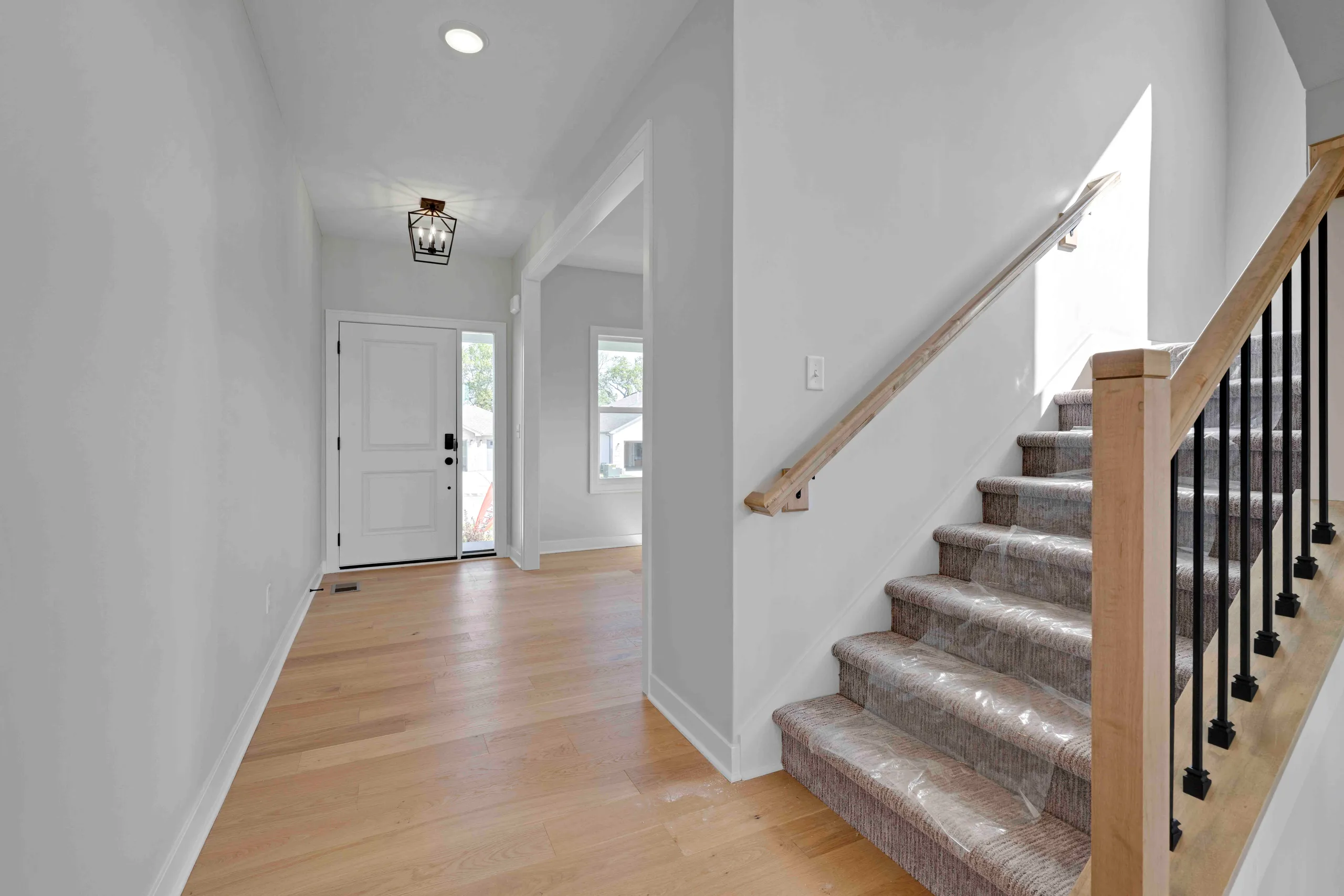 Foyer with white walls, wood flooring, white front door, and staircase with wood railing and patterned runner.