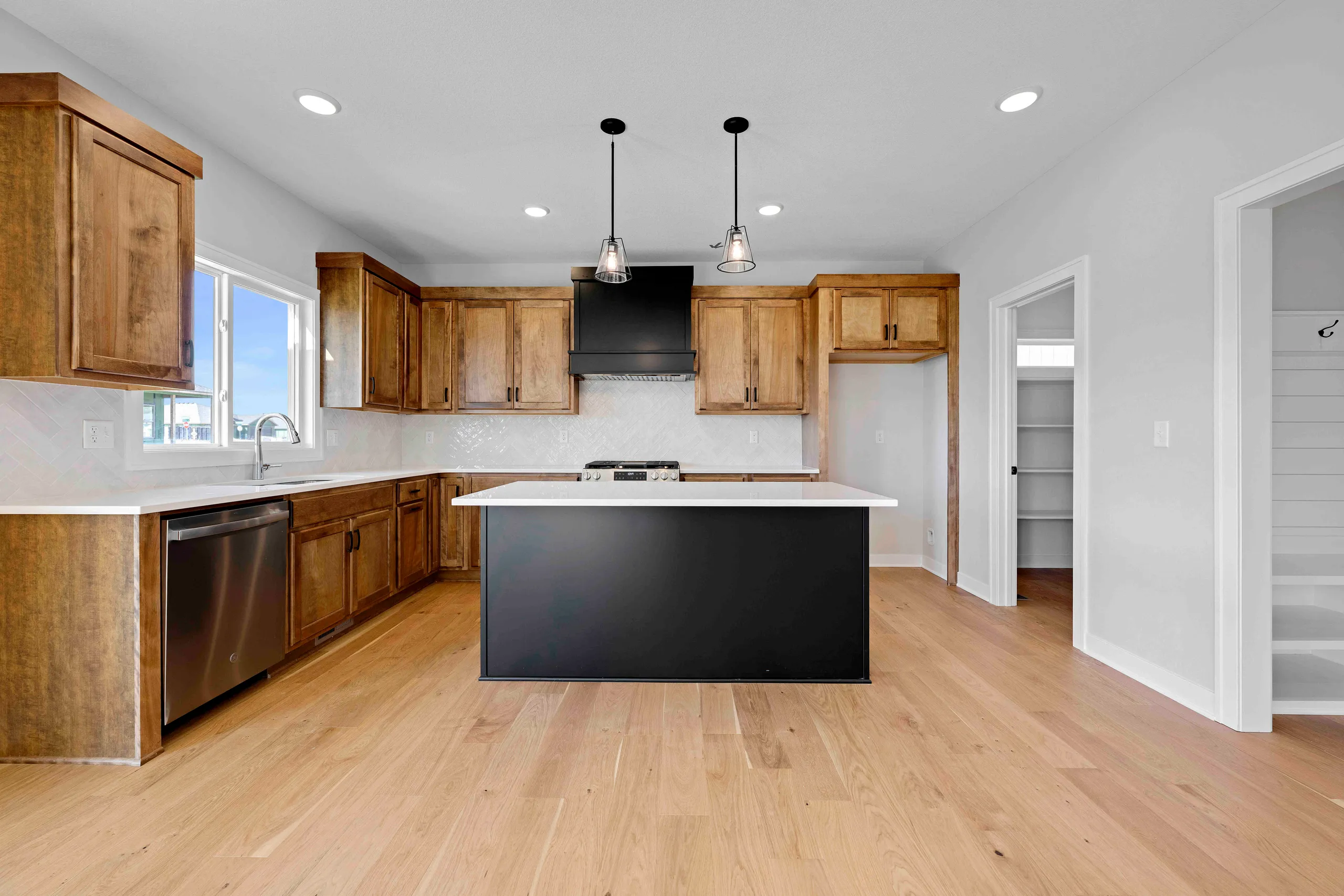 Kitchen with wood cabinets, black island, white countertops, stainless steel appliances, and hardwood floors.