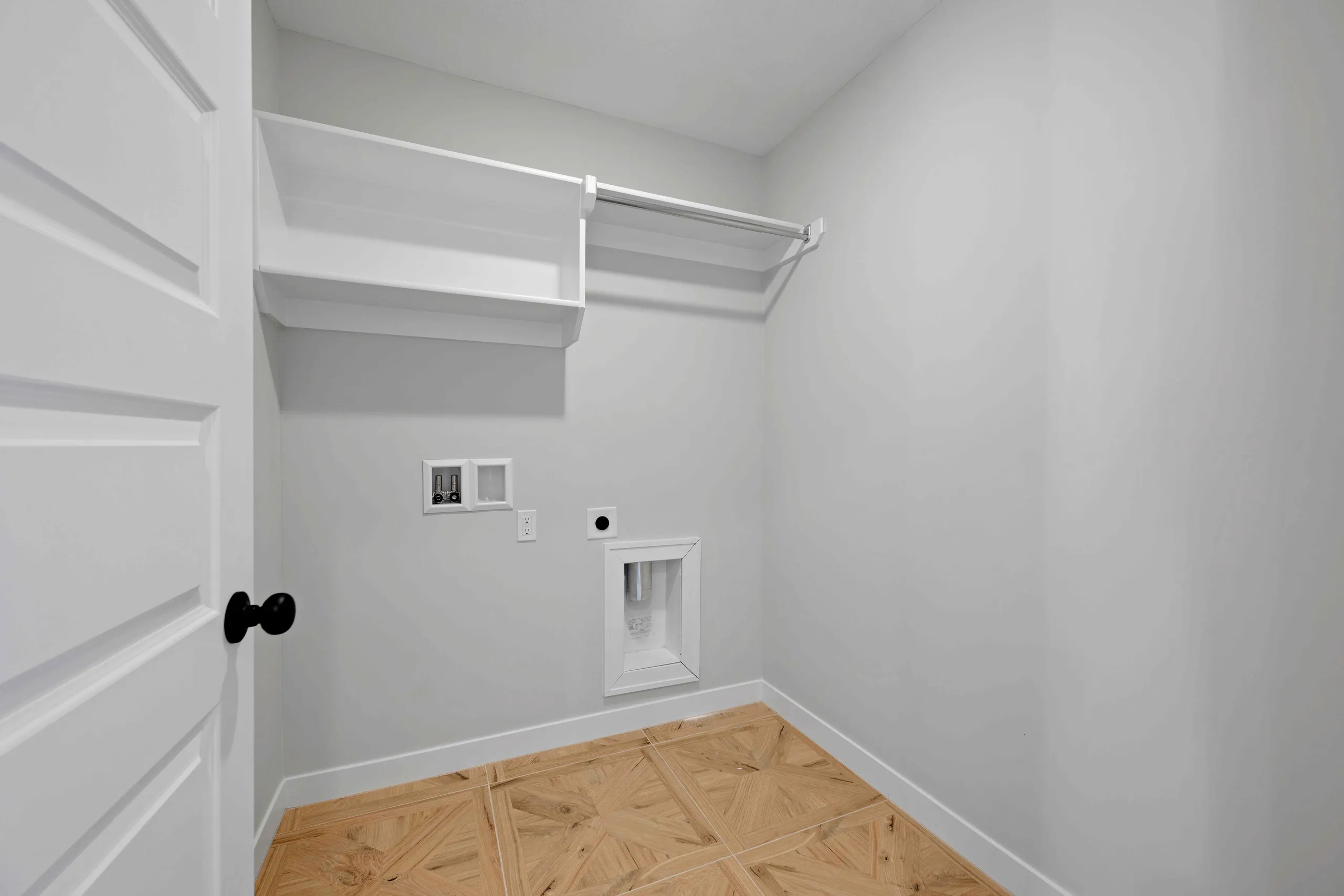 Small closet with white walls, wood plank flooring, metal rod, shelving, and wall outlet.