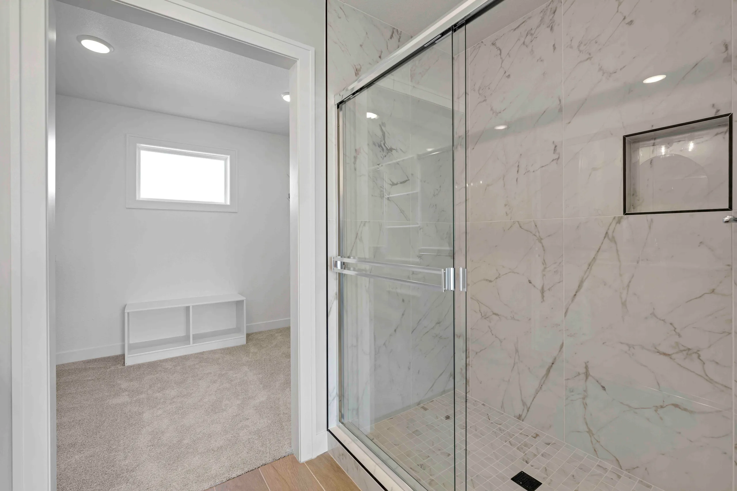 Bathroom with marble-tiled walk-in shower with glass enclosure and adjacent carpeted dressing area with bench seating.