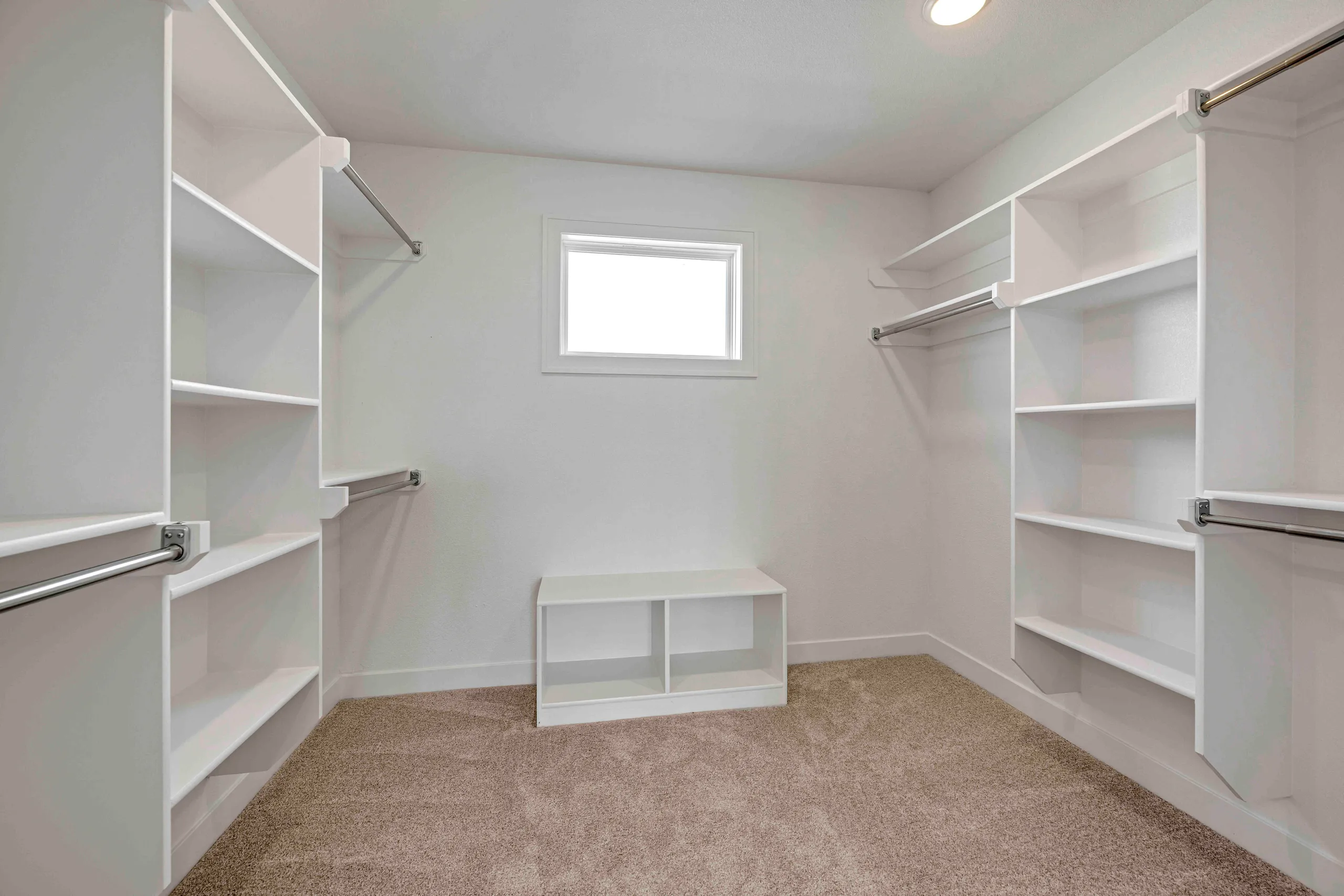 Walk-in closet with white shelving, hanging rods, a central storage bench, and a window.
