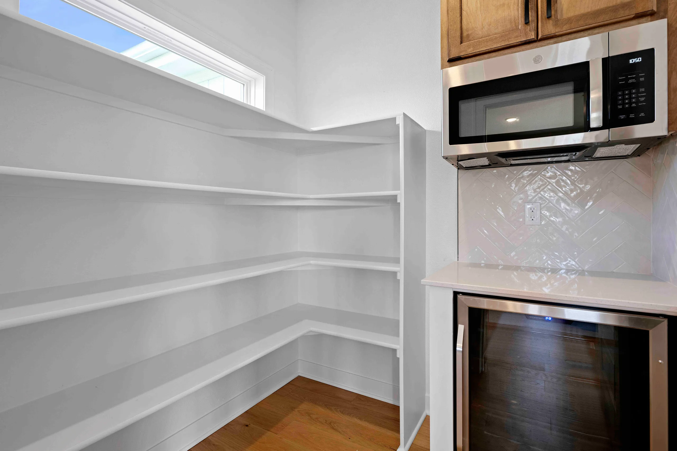 Walk-in pantry with white shelving and wood flooring adjacent to kitchen with stainless steel appliances and white subway
