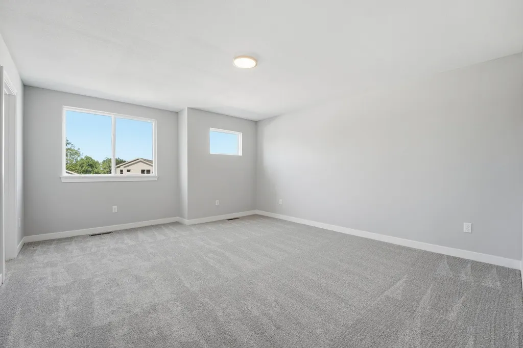 Empty bedroom with gray carpet, white walls, two windows, and recessed ceiling light.