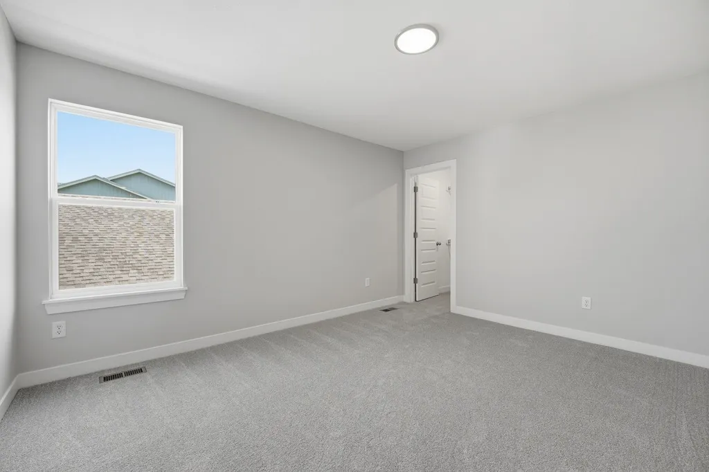Empty bedroom with gray carpet, gray walls, recessed lighting, window with brick exterior view, and white door.