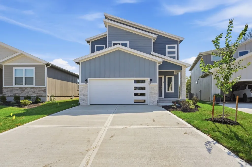 Two-story home with gray and white exterior, white garage door with horizontal stripes, concrete driveway, and landscaped