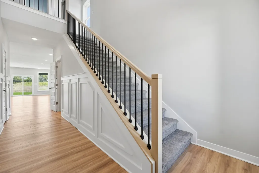 Staircase with black metal balusters, wood handrail, and gray carpeted steps leading to a second-floor landing with white