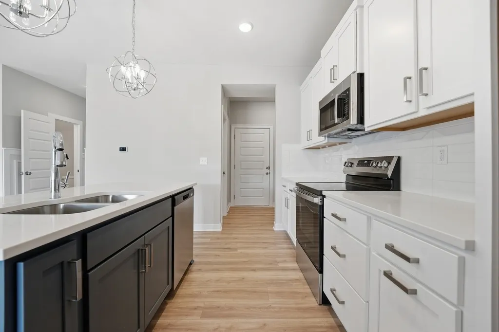 Galley kitchen with white cabinetry, dark island, stainless steel appliances, and wood flooring.