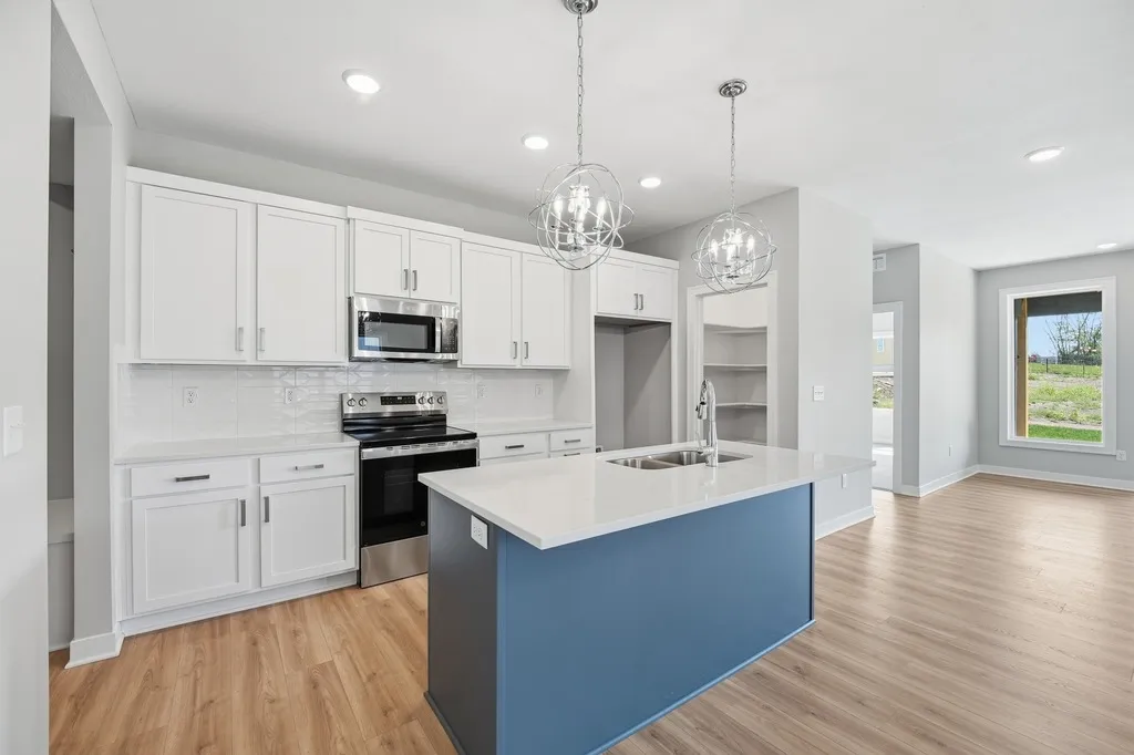 Modern kitchen with white cabinetry, blue island, stainless steel appliances, pendant lights, and wood flooring opening to a