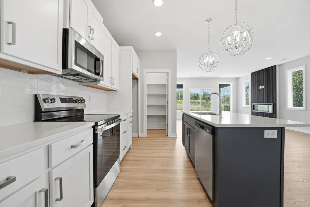 Kitchen with white cabinetry, stainless steel appliances, black island with white countertop, and pendant lights.