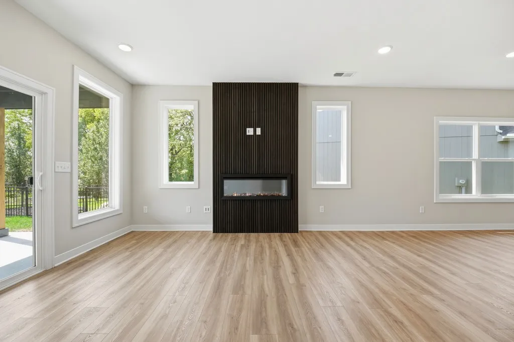 Open living room with wood-look flooring, black vertical shiplap fireplace, and glass doors opening to a deck.