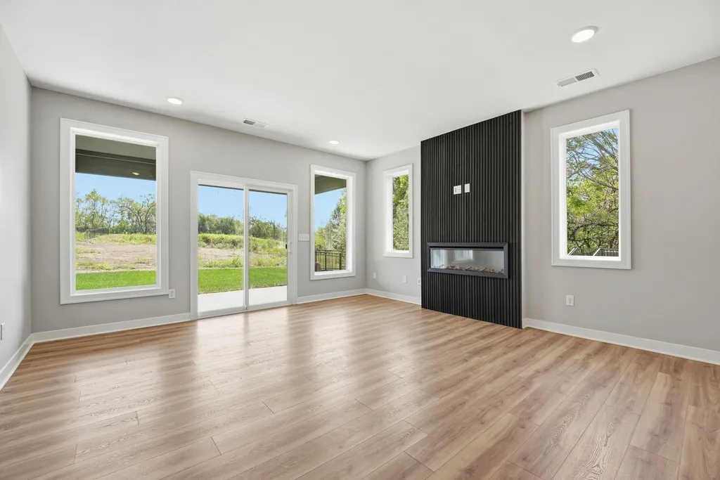 Empty room with wood flooring, gray walls, black accent wall with fireplace, and multiple windows and glass doors