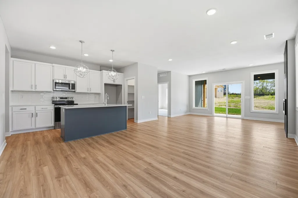 Open-concept kitchen and living area with white cabinetry, dark island, wood flooring, and glass doors overlooking a green
