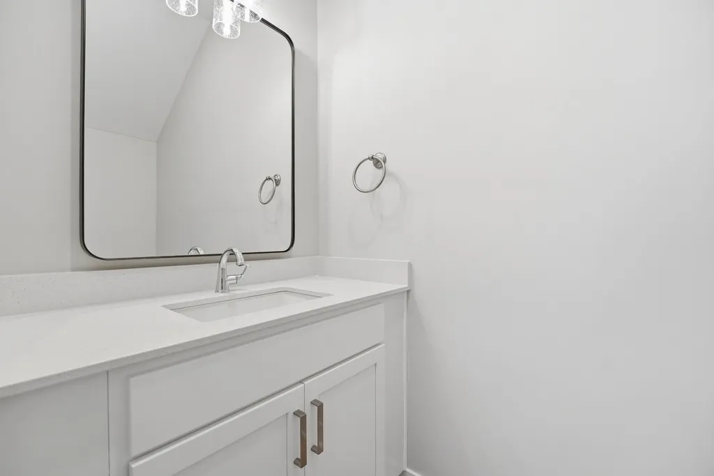 White bathroom vanity with undermount sink, framed mirror, and chrome fixtures.