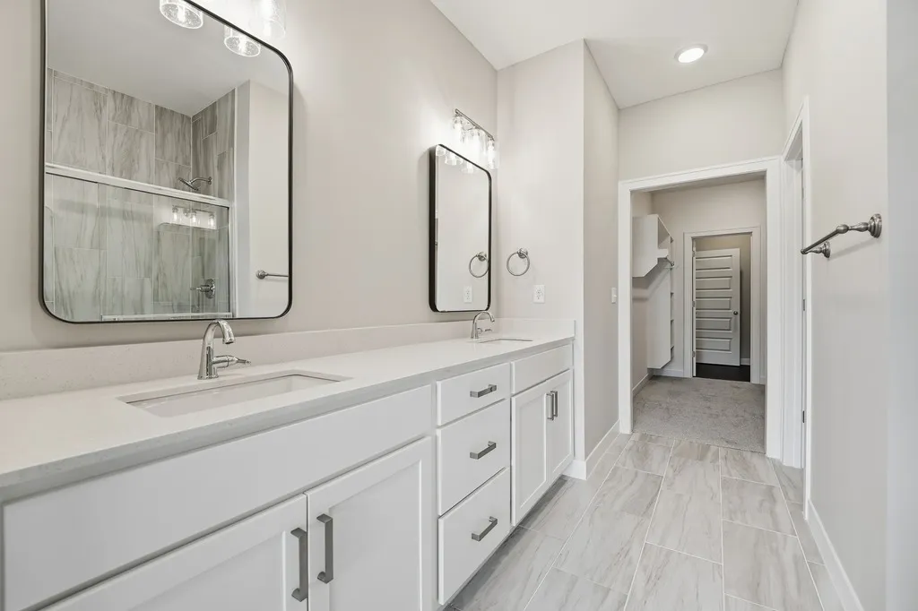 Primary bathroom with double vanity, white cabinetry, quartz countertop, framed mirrors, and tile flooring.