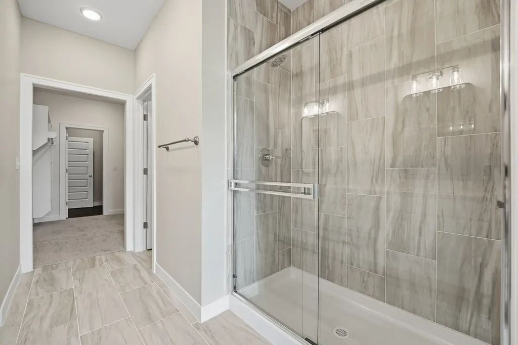 Bathroom with large walk-in shower with glass enclosure and gray tile, connected to hallway with white trim and light gray