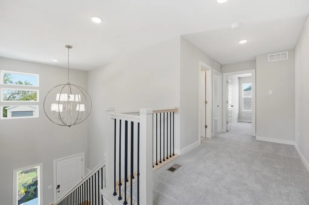 Second-floor hallway with gray carpet, white walls, black spindle railing, pendant light, and multiple doorways leading to