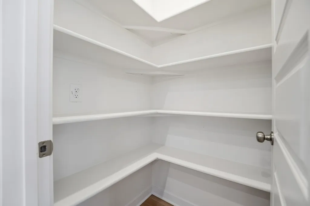 Empty walk-in closet with white shelving, recessed ceiling light, and outlet on wall.