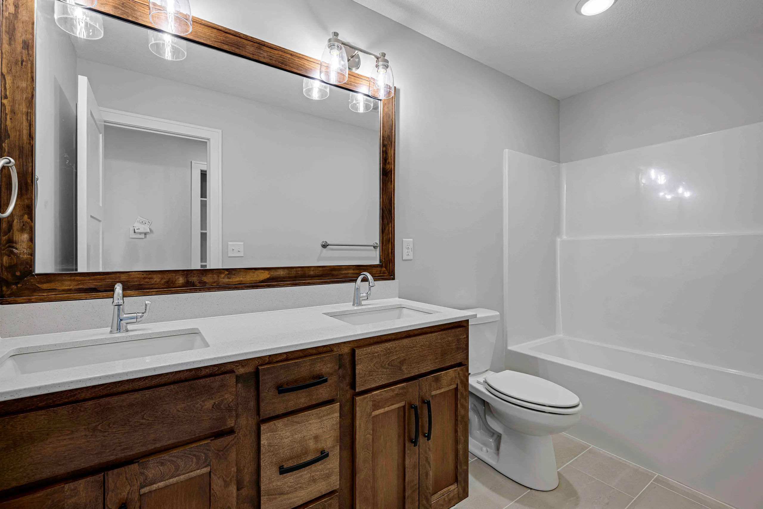 Bathroom with dual sink vanity with dark wood cabinetry, white countertop, large framed mirror with lighting, and white