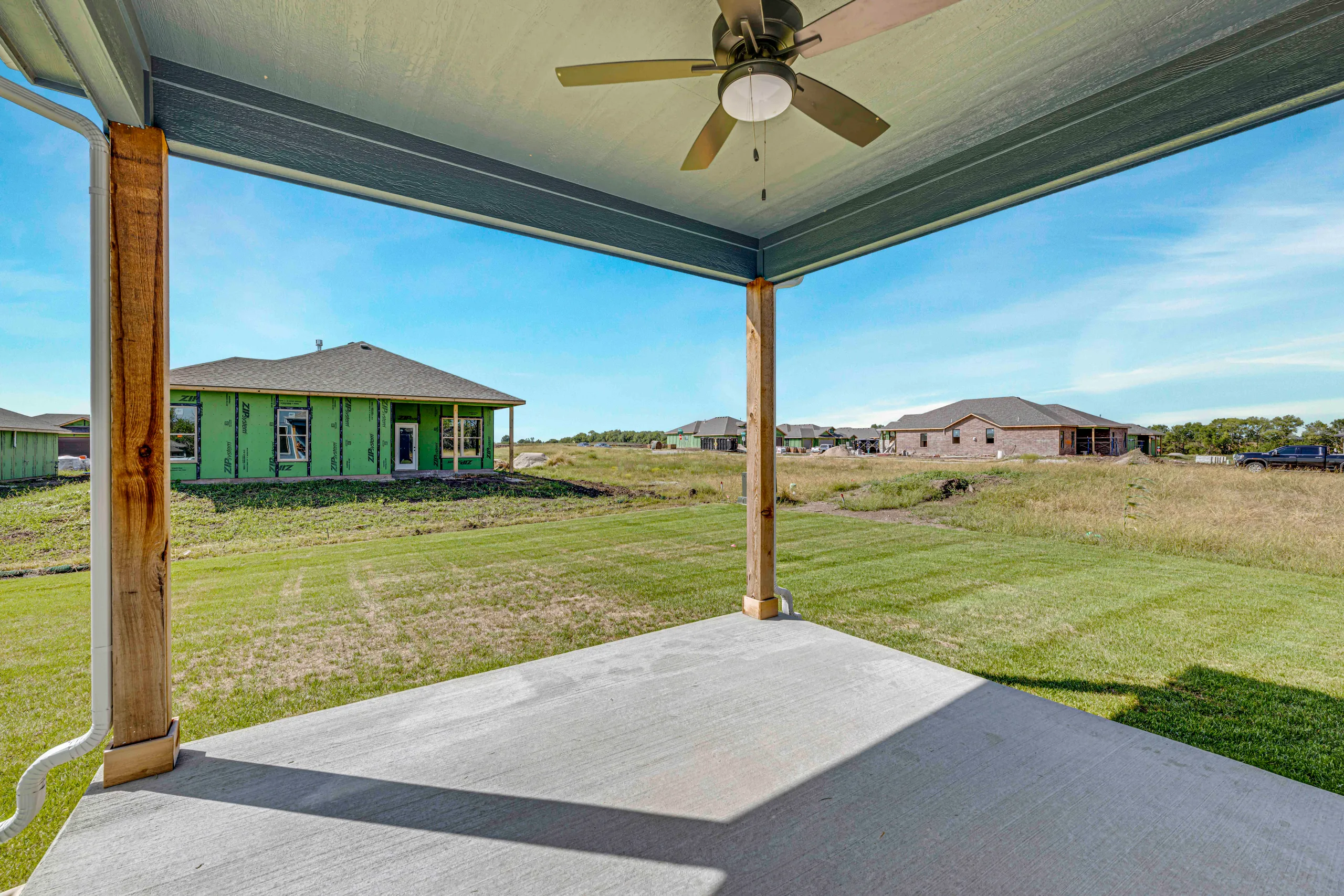 Covered patio with ceiling fan overlooking green lawn and neighboring homes in a residential community.