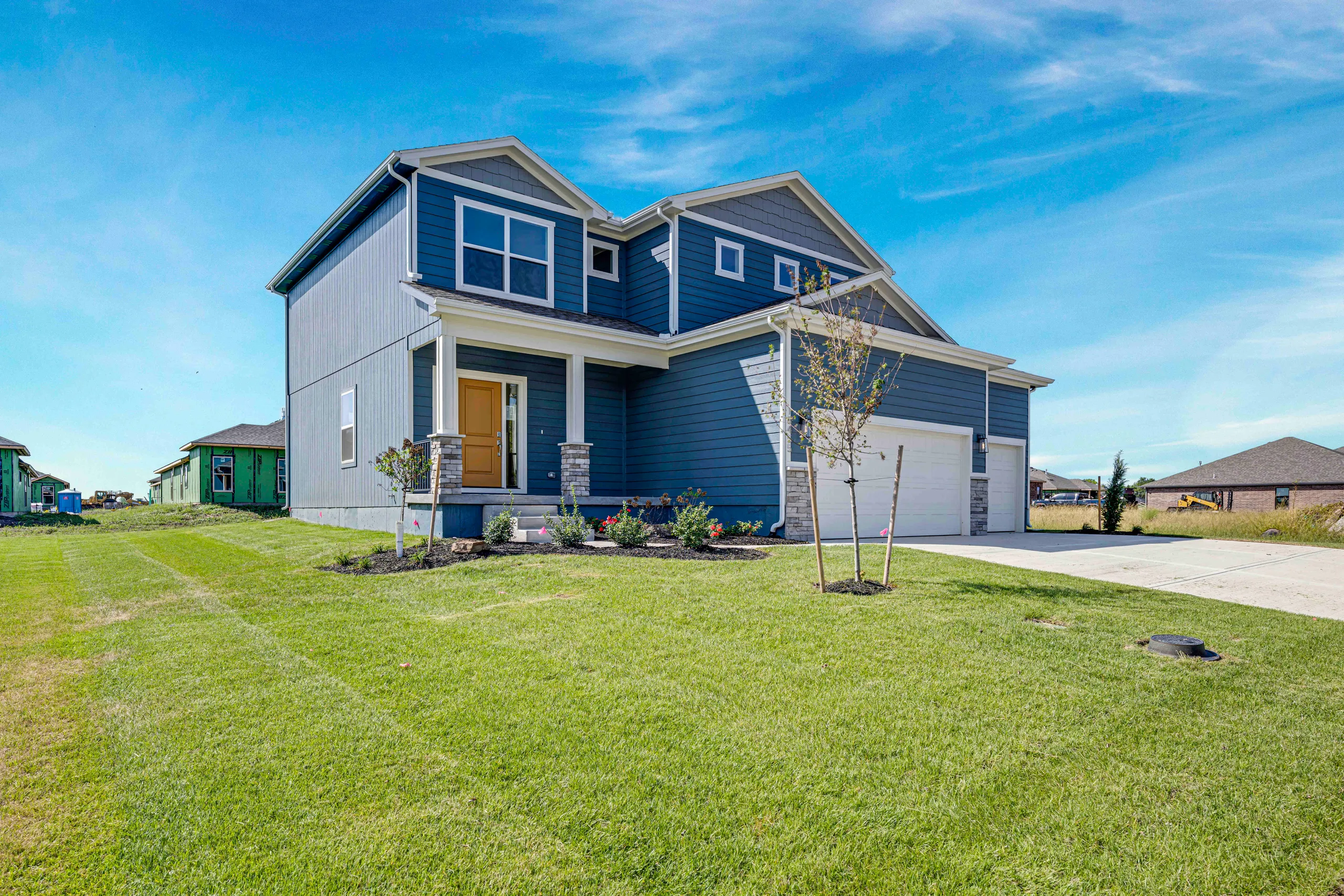 Two-story home with blue siding, gabled roof, yellow front door, and attached garage on manicured lawn.
