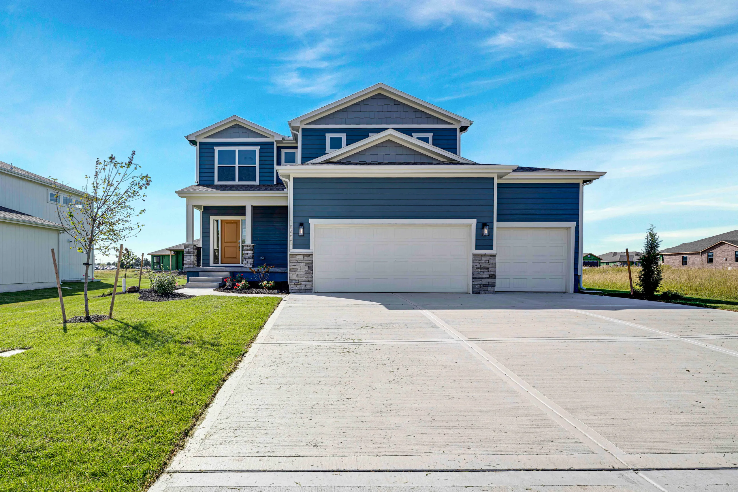 Two-story blue house with white trim, two-car garage, and concrete driveway on a grassy lot.