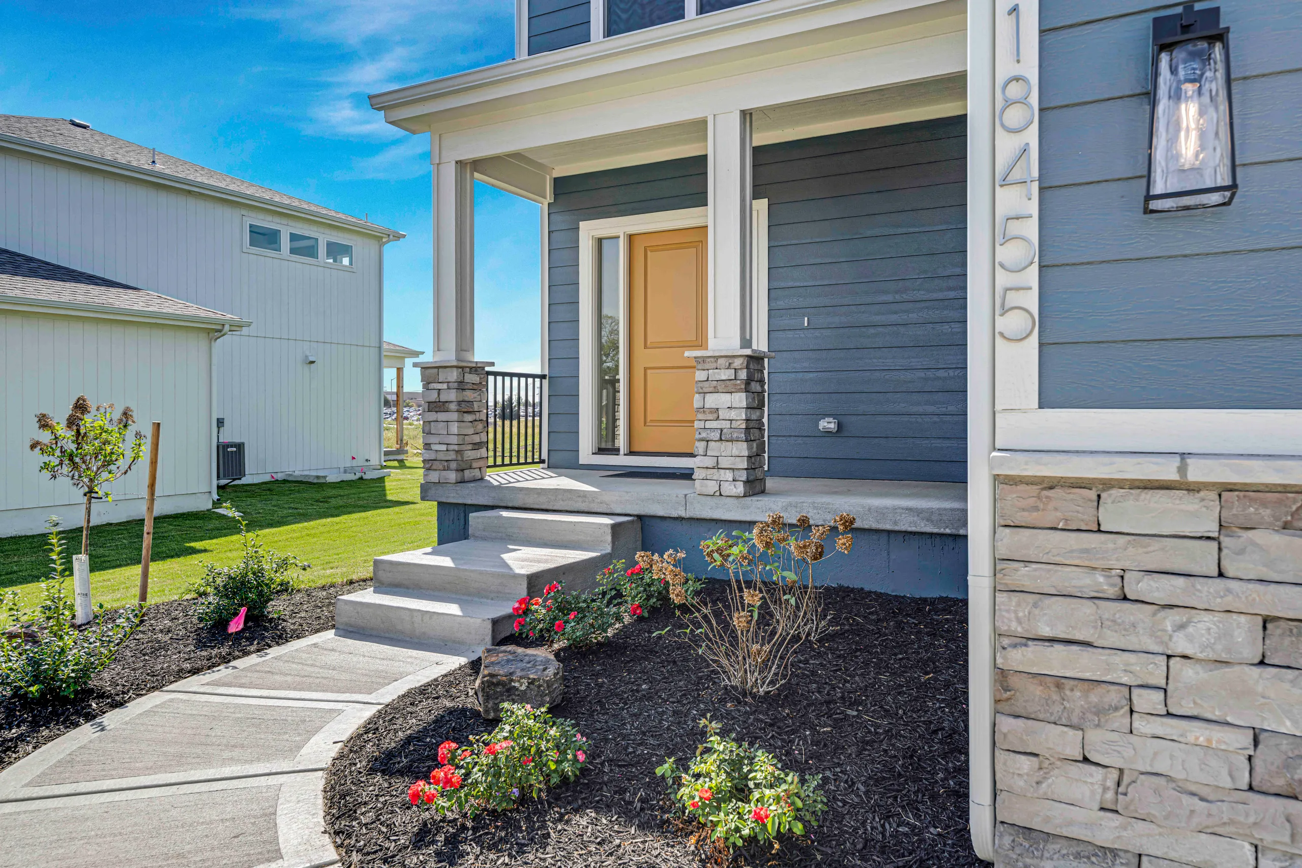 Home exterior with blue siding, yellow front door, stone columns, and landscaped entry with flower beds and walkway.